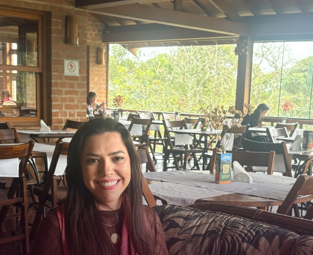 Jaque sorrindo numa varanda de restaurante com mesas e muito verde ao fundo